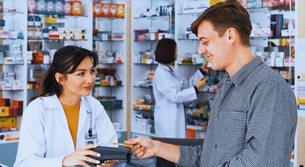 Pharmacien et client au comptoir d'une officine, application carte vitale nouveautés